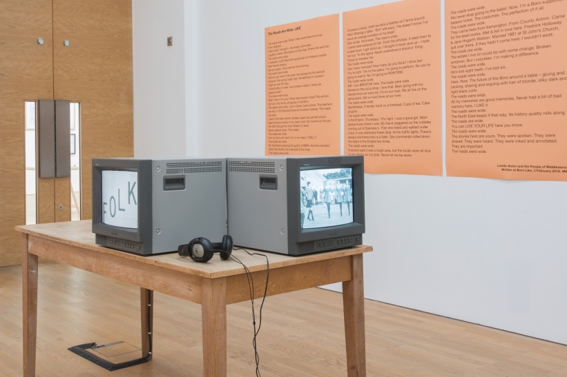 photo description: old fashioned square tv monitors are on a table in front of bright orange boards which have my poem printed on them
